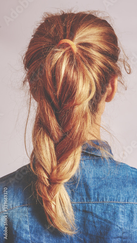 The back view of a young woman with blond hair woven into a sloppy, stylish French-style braid.