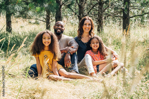 Portrait of happy mixed race family sitting in grass in park in summer