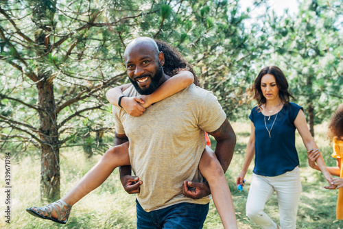 Smiling dad giving daughter piggy pack ride in park with family