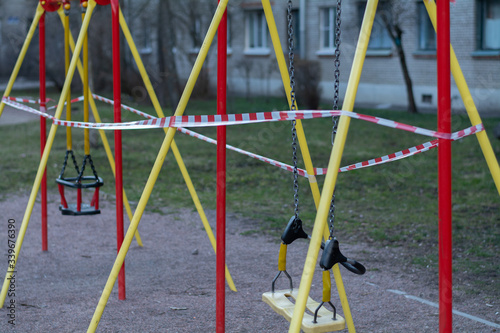 The playground and the swing for children are closed and blocked by a barrier tape due to the covid19 crown virus. A swing on the court cannot be used. Nobody on the swing.