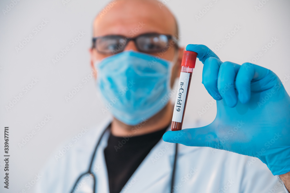 Doctor Holding Pandemic Coronavirus 2019-nCoV Blood Sample Positive Test Tube. Doctor wearing medical mask and gloves and shows patient's blood test tube containing corona virus (COVID-19)
