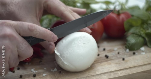 Tagliare una mozzarella di bufala sul tagliere per preparare una caprese: ricetta italiana