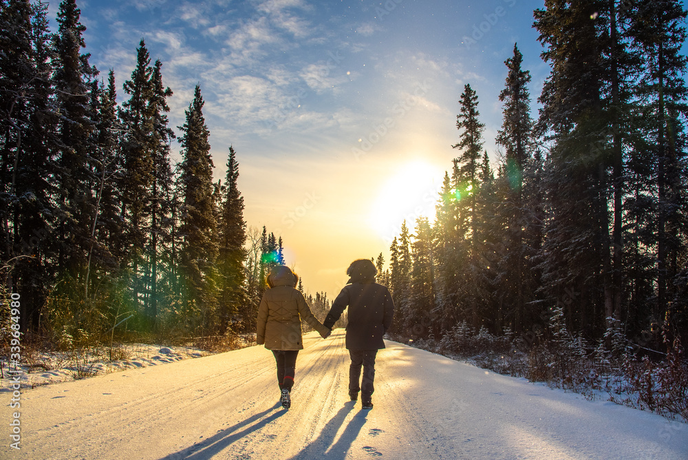 Couple walking along winter, snowy road in freezing temperatures.  Couple, love, holding hands walking. 