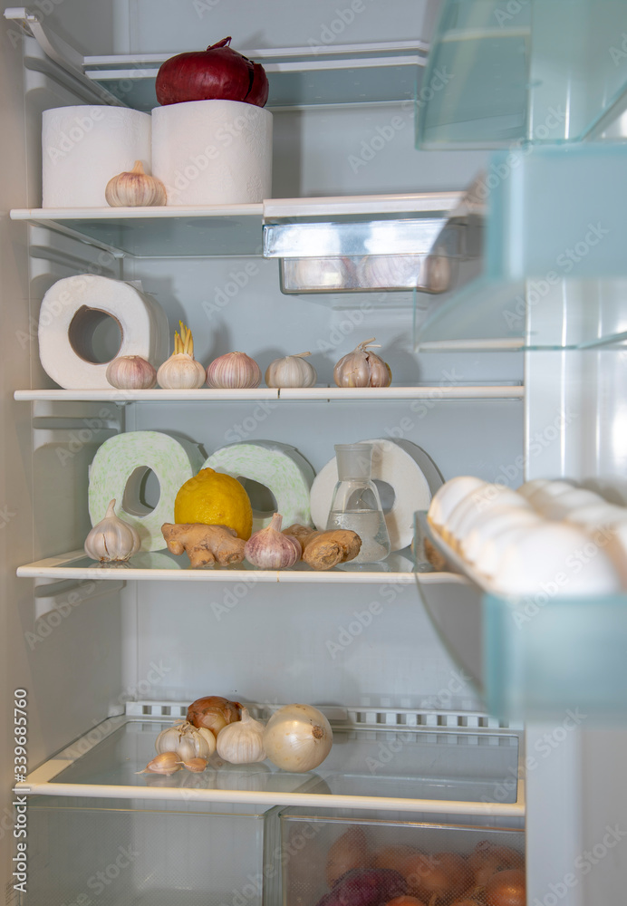 There are rolls of toilet paper, garlic , ginger, and eggs in the open refrigerator.