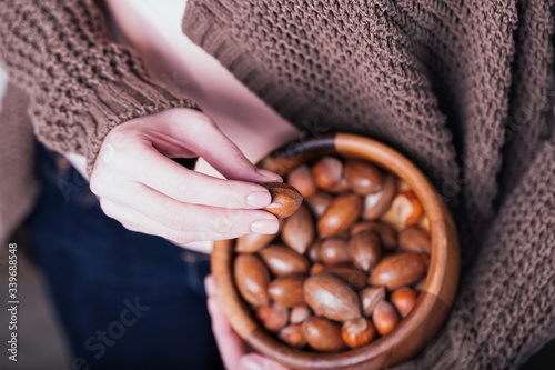Female hands holding wooden bowl with pecan nuts and hazelnuts on knitted sweater background
