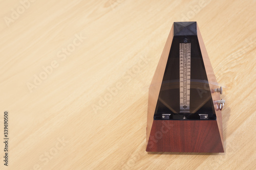 musical metronome with pendulum in motion and wooden background with space for horizontal banner.