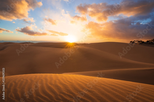 Sunset in the desert  sun and sun rays  Beautiful clouds on blue sky. Golden sand dunes in desert in Maspalomas  Gran Canaria  Canary islands  Spain 