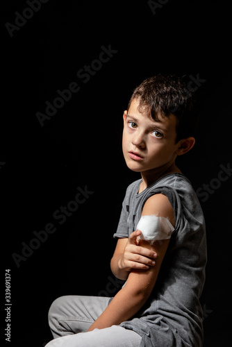 Cute little boy with sticking plaster on arm on black background