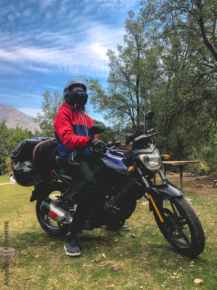 Fototapeta premium Guy with red and blue jacket and black motorcycle and helmet at chilean countryside, Cajón del Maipo, Chile