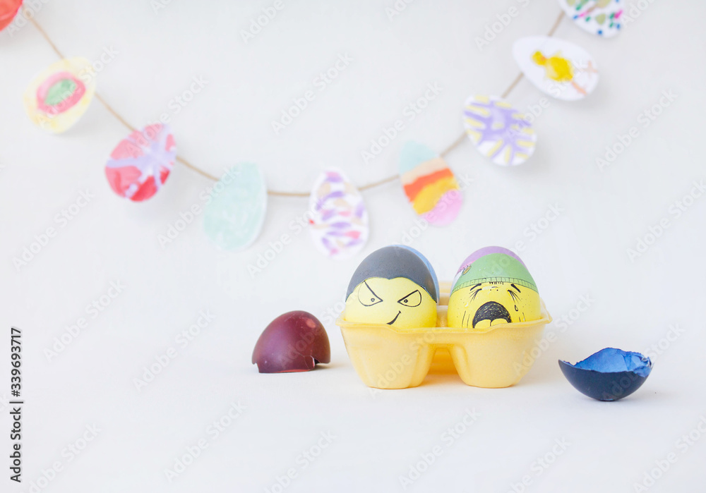 On a yellow stand are painted eggs on a white background. Real hand-painted eggs. A multi-faceted photo. The white photo has funny cute faces on the eggs. Holiday and joy of Bright Easter
