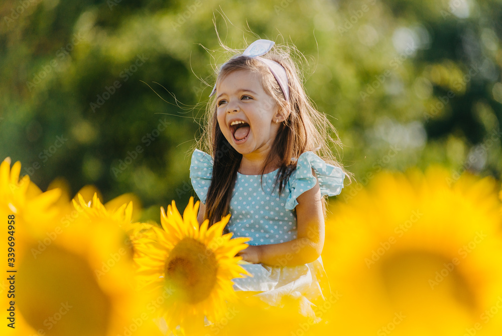 Little cheerful girl in a field of yellow sunflowers. Child and ...