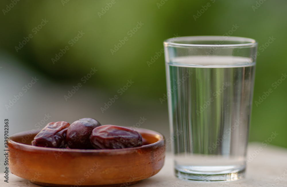 A glass of water and iftar dry dates on plate ready to eat for iftar time. Islamic religion and ramadan concept. Natural blured background with copy space. A glass of water and iftar dry dates on plate ready to eat for iftar time. Islamic religion and ramadan concept. Natural blured background with copy space.