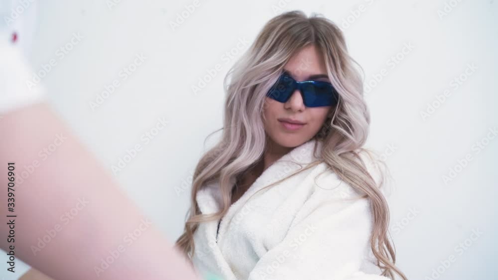 CU: beautiful young woman with blonde hair in bathrobe undergoes laser epilation procedure in cosmetic clinic closeup CU: beautiful young woman with blonde hair in bathrobe undergoes laser epilation procedure in cosmetic clinic closeup