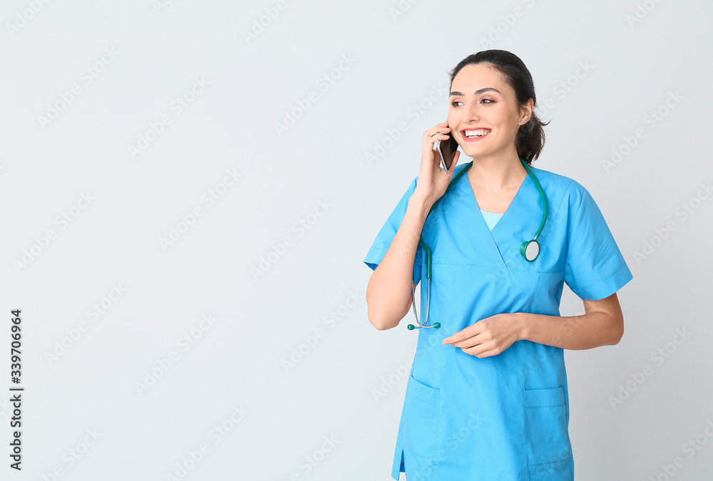 Portrait of young female doctor talking by phone on light background Portrait of young female doctor talking by phone on light background