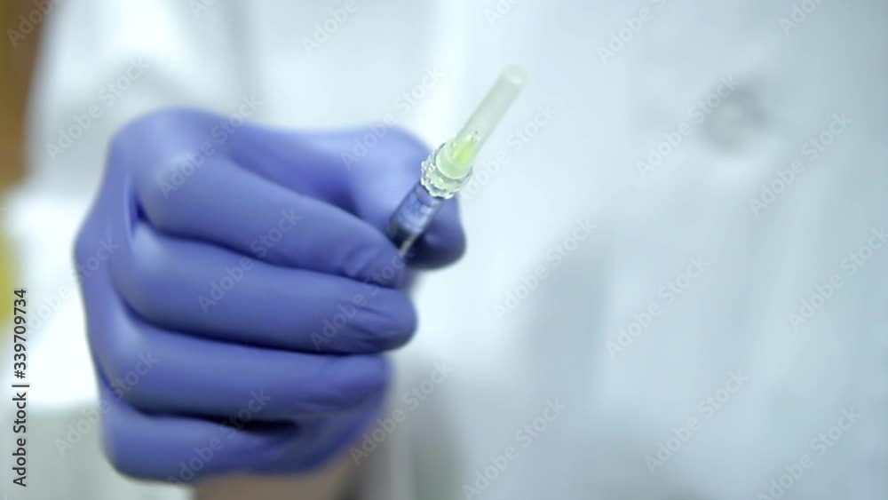 A cosmetologist’s hands in purple rubber gloves holding syringe with a needle for rejuvenating facial injections. A cosmetologist’s hands in purple rubber gloves holding syringe with a needle for rejuvenating facial injections.