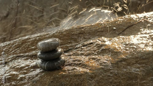Stack of stones balancing on wet surface on a background of splashing waterfall in the sunlight