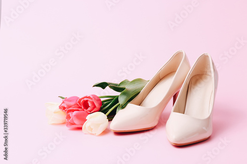 Female high heel shoes with beautiful tulips on pink background