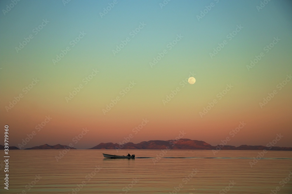 Pescador cruzando en  lancha con luna llena en fondo en alba