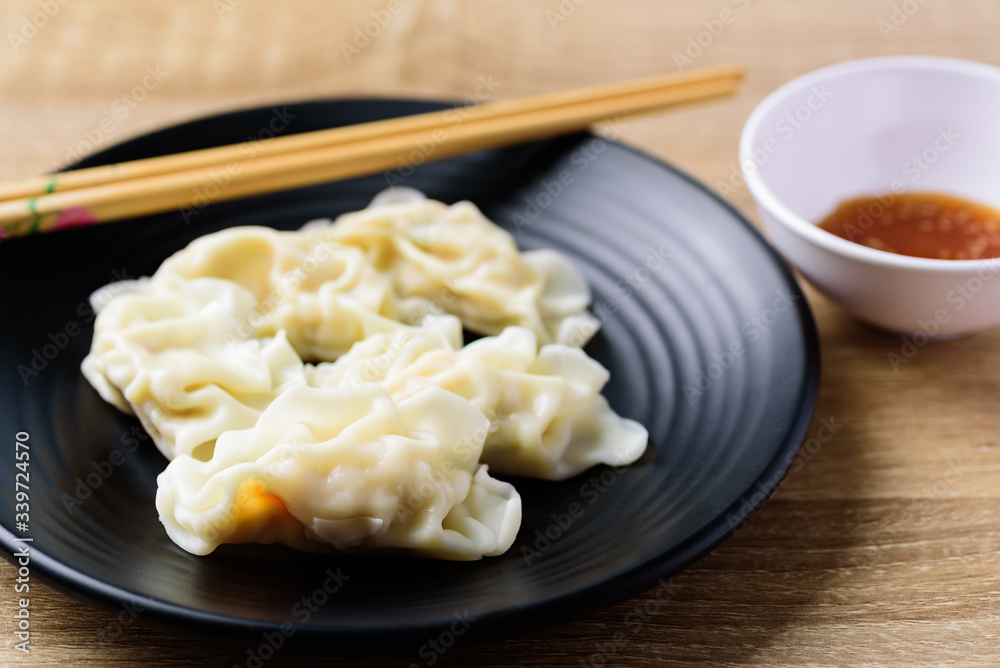 Steamed wonton dumpling stuffed with minced pork and shrimp on black plate and chopsticks, Asian food Steamed wonton dumpling stuffed with minced pork and shrimp on black plate and chopsticks, Asian food