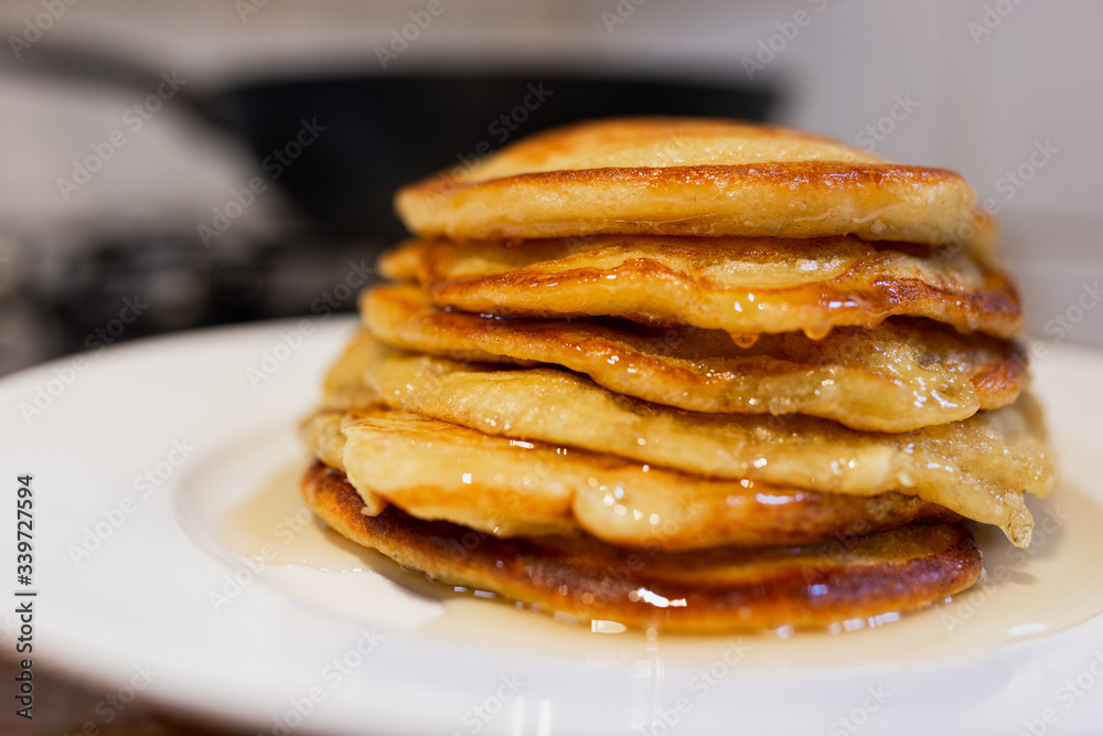 Fresh homemade classic pancakes with maple syrup in a white plate on a wooden board with a pan in the background. Fresh homemade classic pancakes with maple syrup in a white plate on a wooden board with a pan in the background.