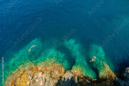 A cenital view of some people swimming in the sea with a rocky coastline.