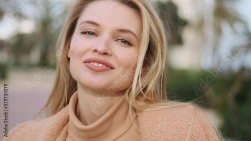 Portrait of charming blond girl happily looking in camera and smiling on street
