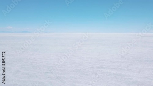 Drone footage of a girl walking on the Salar de Uyuni Salt Flat in Bolivia wearing a yellow coat