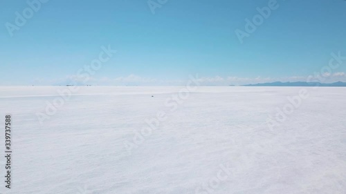 Drone footage of a girl walking on the Salar de Uyuni Salt Flat in Bolivia wearing a yellow coat