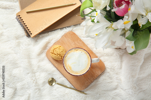 Cup of coffee, flowers, cookie and notebook on soft plaid