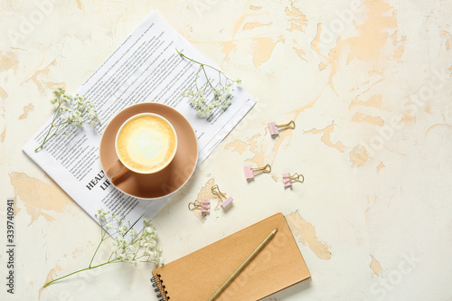 Cup of coffee, notebook, newspaper and flowers on light background