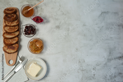 Delicious homemade Breakfast. French toast, butter, slices of stewed apples, strawberry jam, cherry sauce and honey on a gray concrete background. Free space.