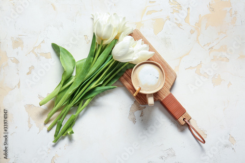 Cup of coffee and bouquet of flowers on light background