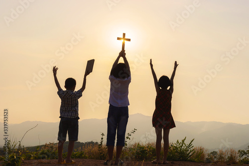 Bild auf Leinwand Silhouette of children praying to the GOD while holding a crucifix symbol with b