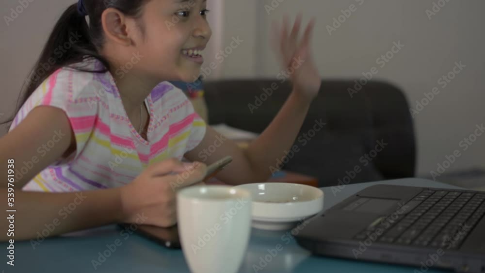 Asian cute girl playing games from mobile phone at home during COVID-19 pandemic situation. Female teenager greeting her friend from computer laptop with social online communication during quarantine. Asian cute girl playing games from mobile phone at home during COVID-19 pandemic situation. Female teenager greeting her friend from computer laptop with social online communication during quarantine.
