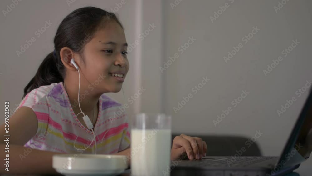Female teenager studying from home with video call during COVID-19 pandemic situation. Asian cute girl drinking fresh milk while talking with teacher from laptop during learning lesson online. Female teenager studying from home with video call during COVID-19 pandemic situation. Asian cute girl drinking fresh milk while talking with teacher from laptop during learning lesson online.