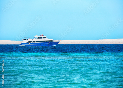 Boat with tourists sailing Red Sea, long view. Blue water under clear blue sky. Photographed in Egypt. Selective soft focus. Blurred background