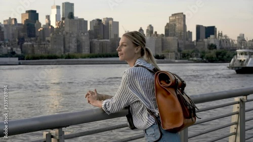 Attractive female traveller with touristic backpack using Tower Optical viewer for looking around metropolitan skyline buildings, young hipster girl with retro technology on neck exploring city
