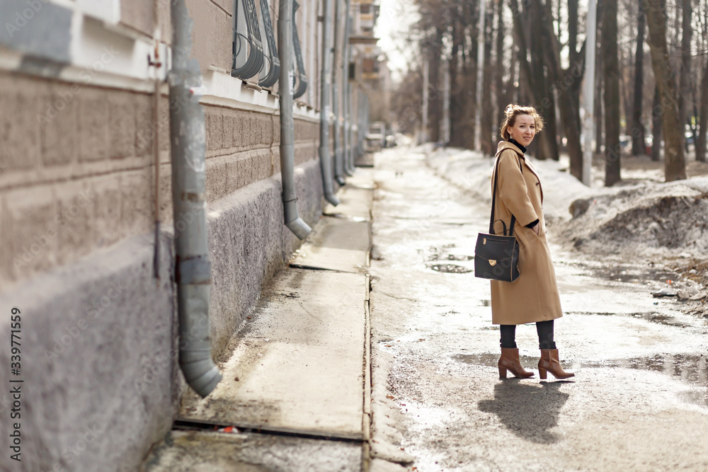young beautiful girl in a beige coat, dressed in a hipster style, enjoys the spring weather and the sun, walks around the city one spring morning young beautiful girl in a beige coat, dressed in a hipster style, enjoys the spring weather and the sun, walks around the city one spring morning