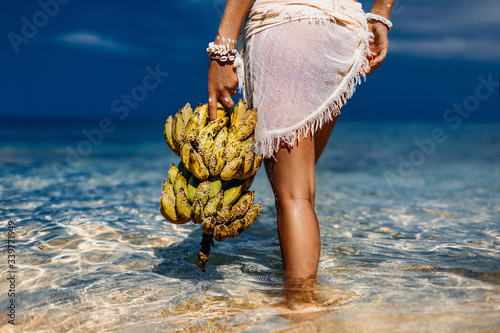 close up of woman holding bunch of banans on the beach photo