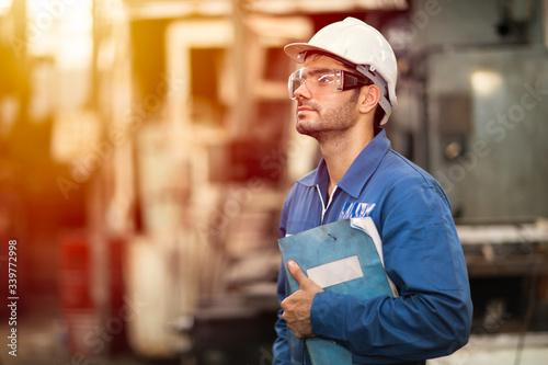 Portrait of smart engineer education machine service manual book happy worker standing proudly in heavy industry background.
