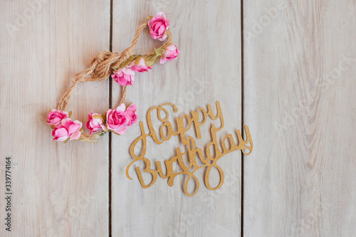 Happy birthday lettering on white wooden background with pink flowers. 