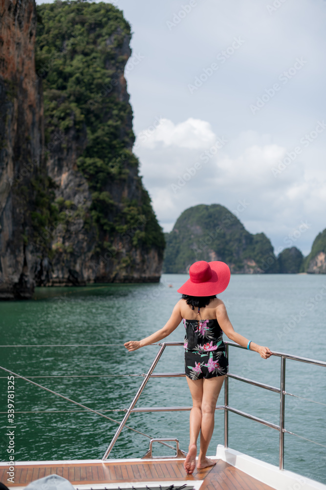 Woman with tropical dress and red hat enjoy beautiful view of ocean and tropical islands from deck of sailing yacht in Phang Nga bay near Phuket Thailand. 