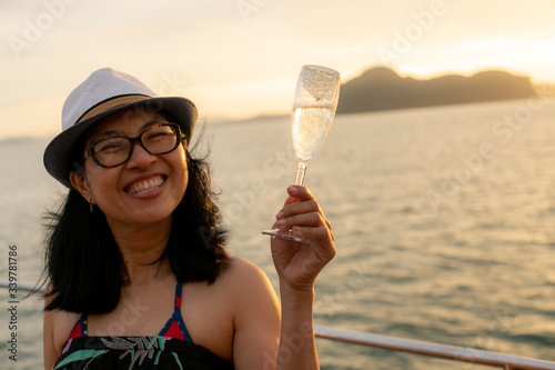 Obraz na płótnie Happy woman on yacht hold a glass of sparkling wine in her hand with background of golden sunset moment to celebrate her life and happiness. w salonie