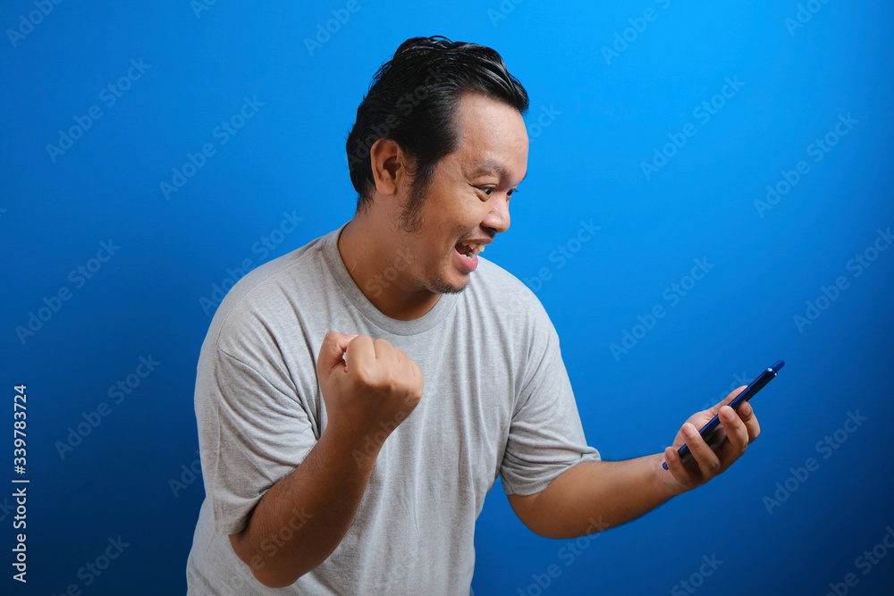 Fat Asian guy wearing a gray T-shirt looks happy over the good news he received from his smartphone Fat Asian guy wearing a gray T-shirt looks happy over the good news he received from his smartphone
