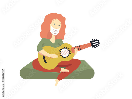 A girl in a medical mask plays the guitar during quarantine on a mattress