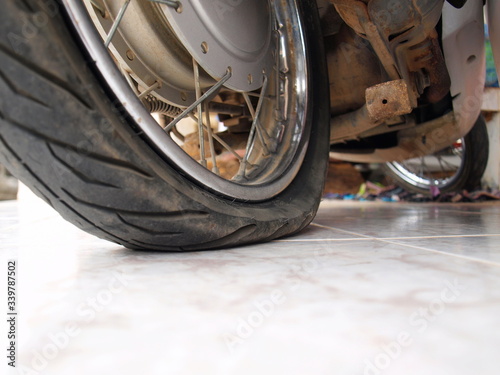Flat tire motorcycle: condition of leaking tires, no air in silver wheels with copy area On a blurred tile background. Selective focus