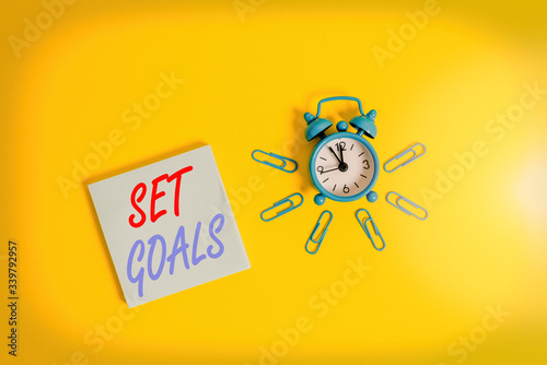 Conceptual hand writing showing Set Goals. Concept meaning Defining or achieving something in the future based on plan Metal vintage alarm clock clips notepad colored background photo