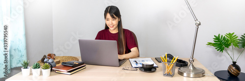 A young, beautiful relaxing business asian girl use a laptop working remotely from home on desk as a freelancer, quarantine for Coronavirus and smart working concept.