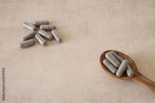 Green herb pills in wooden spoon on beige background photo