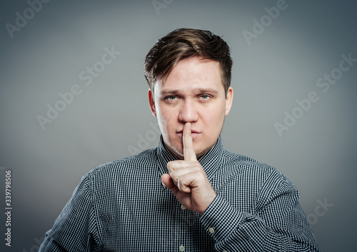 Studio portrait of a young man making a silence gesture, gray background